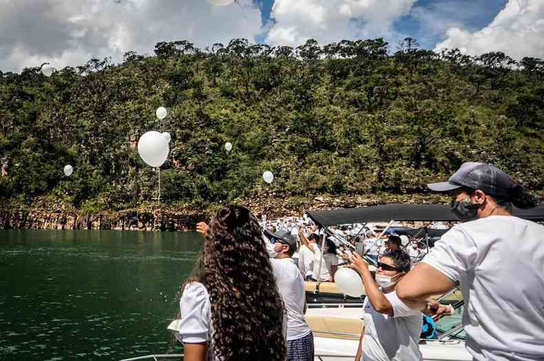 Pessoas em lanchas com roupas brancas soltam bales brancos para o Lago em homenagem s vitimas 
