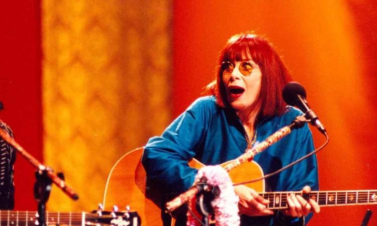 Rita Lee no palco, sentada, segurando violo 