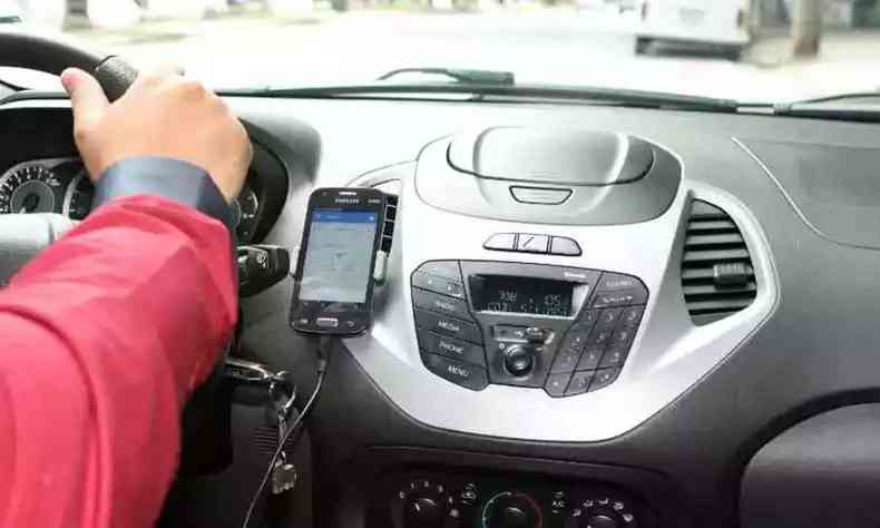 Na foto, motorista de aplicativo segura volante enquanto celular mostra GPS