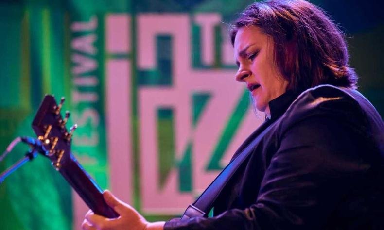 Cantora Madeleine Peyroux, de perfil, toca guitarra no palco