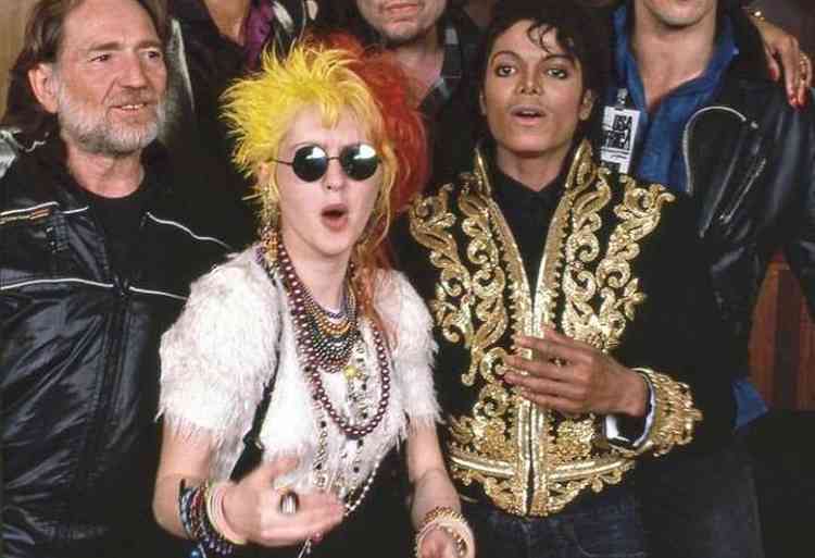 Cyndi Lauper, de cabelo amarelo e vermelho ao lado de Michael Jackson, de jaqueta preta e dourada